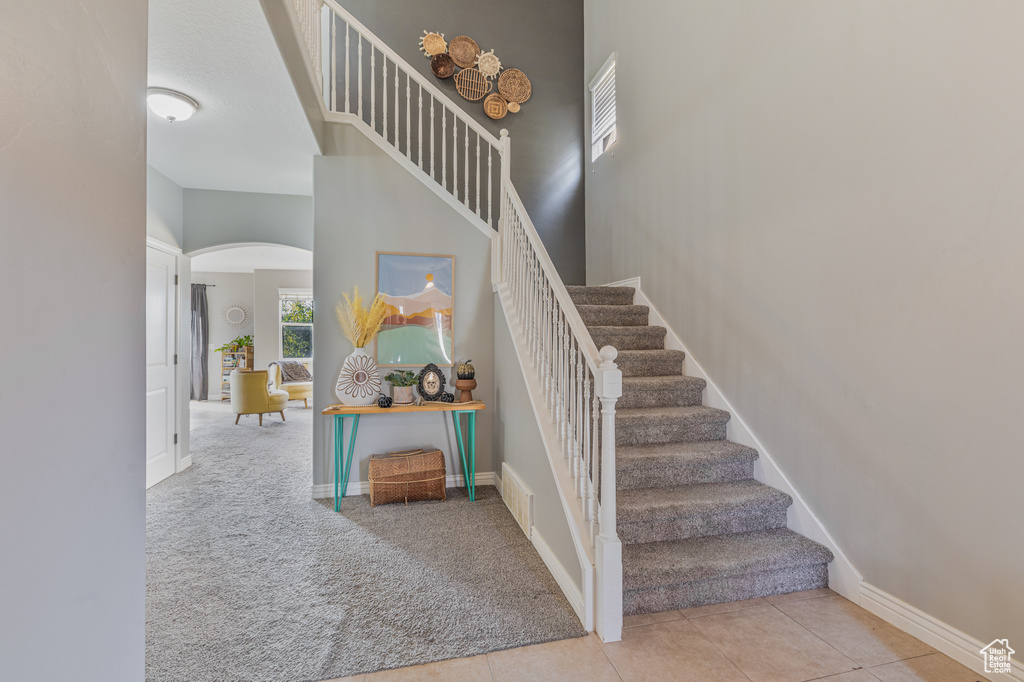 Staircase featuring arched walkways, carpet floors, baseboards, tile patterned flooring, and a towering ceiling