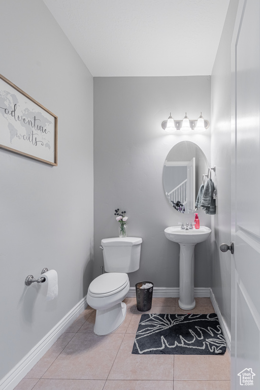 Half bathroom with toilet, tile patterned floors, baseboards, and a sink