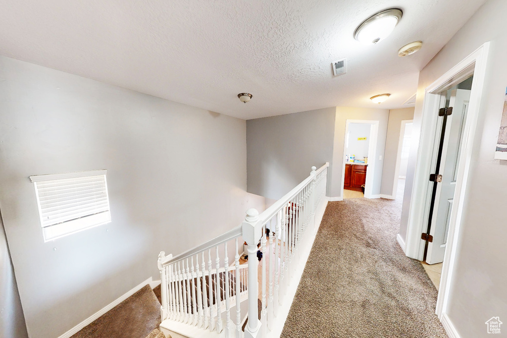 Hall featuring an upstairs landing, light colored carpet, a textured ceiling, and baseboards