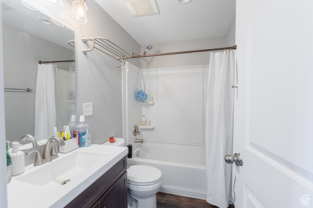 Bathroom featuring vanity, shower / bathtub combination with curtain, wood finished floors, toilet, and a textured ceiling