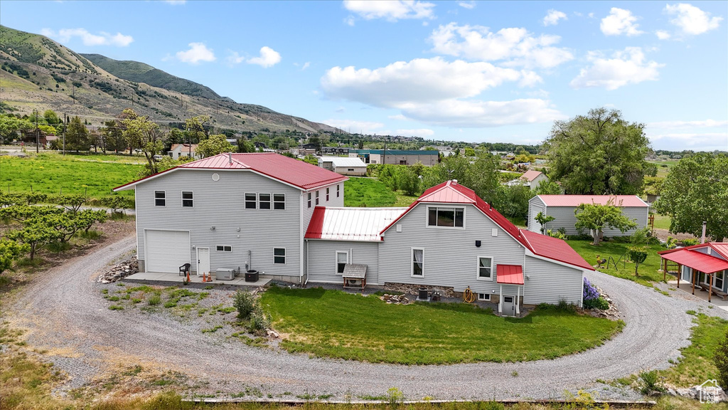 Back of property with dirt driveway, a mountain view, metal roof, a lawn, and a garage