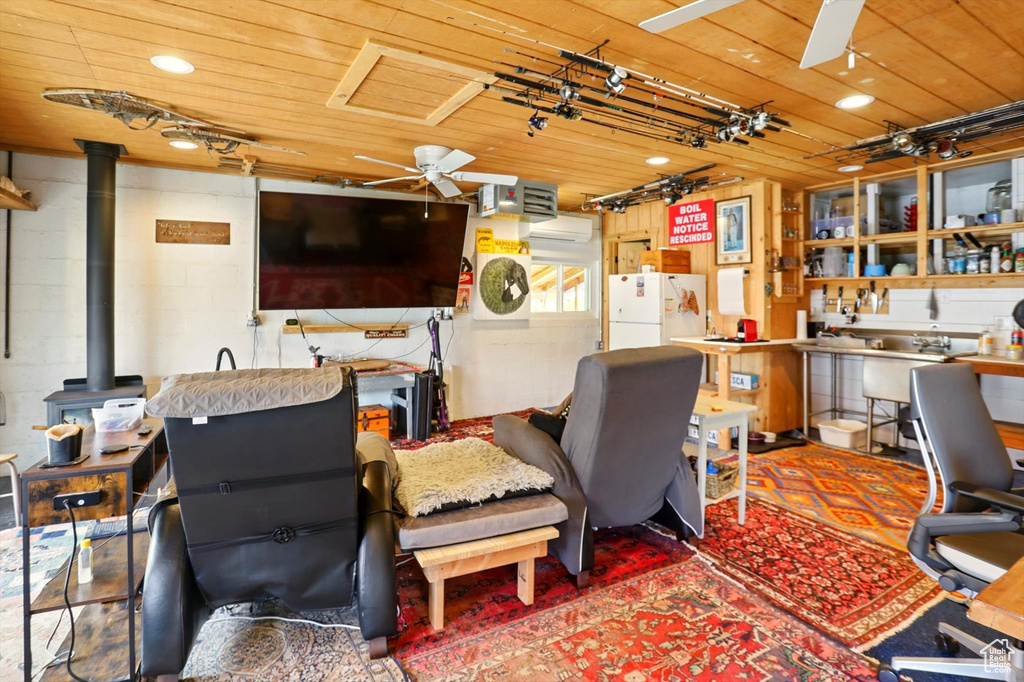 Office area with ceiling fan, a wood stove, wooden ceiling, and concrete block wall