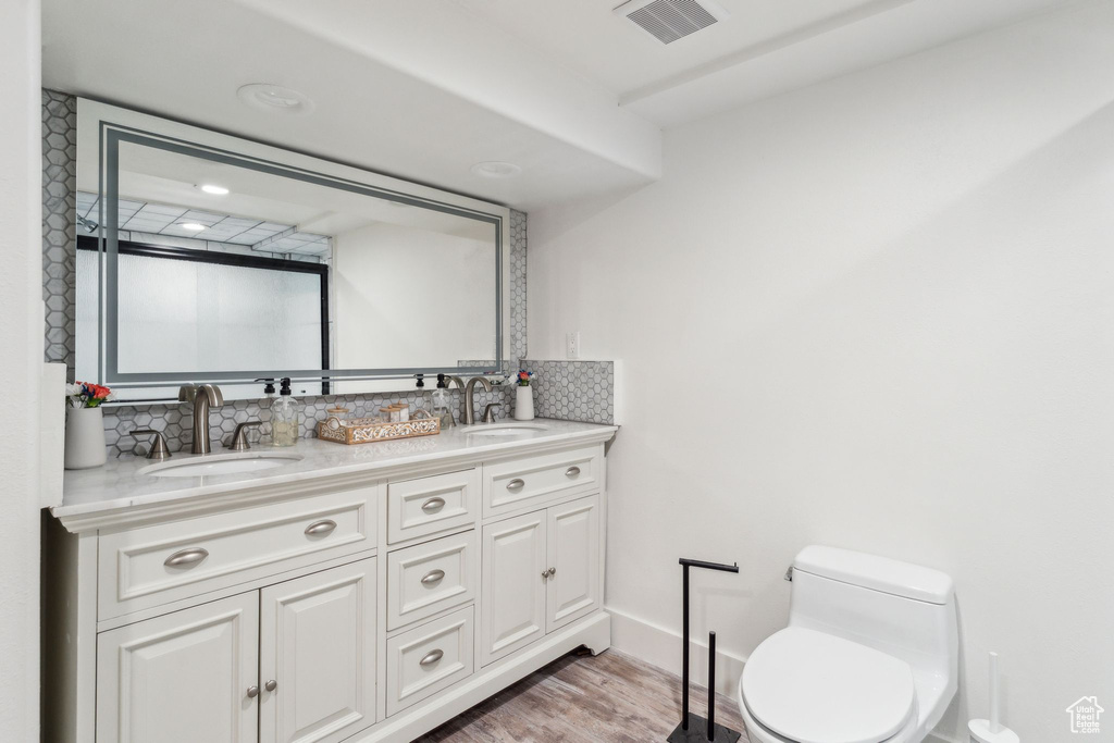Bathroom with decorative backsplash, double vanity, toilet, and wood finished floors