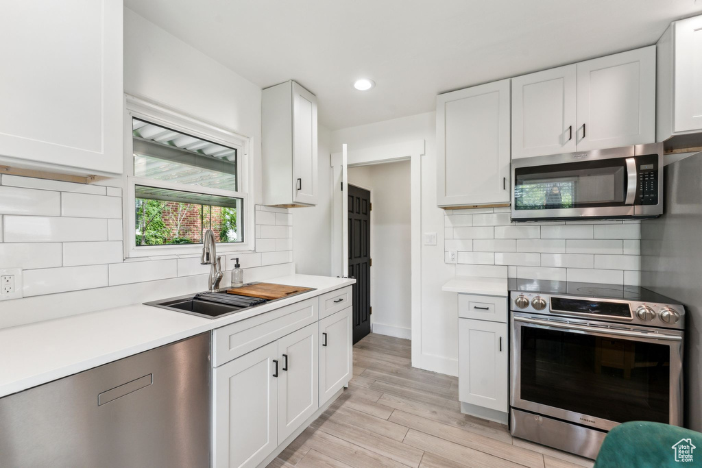 Kitchen featuring stainless steel appliances, a sink, light countertops, white cabinets, and tasteful backsplash