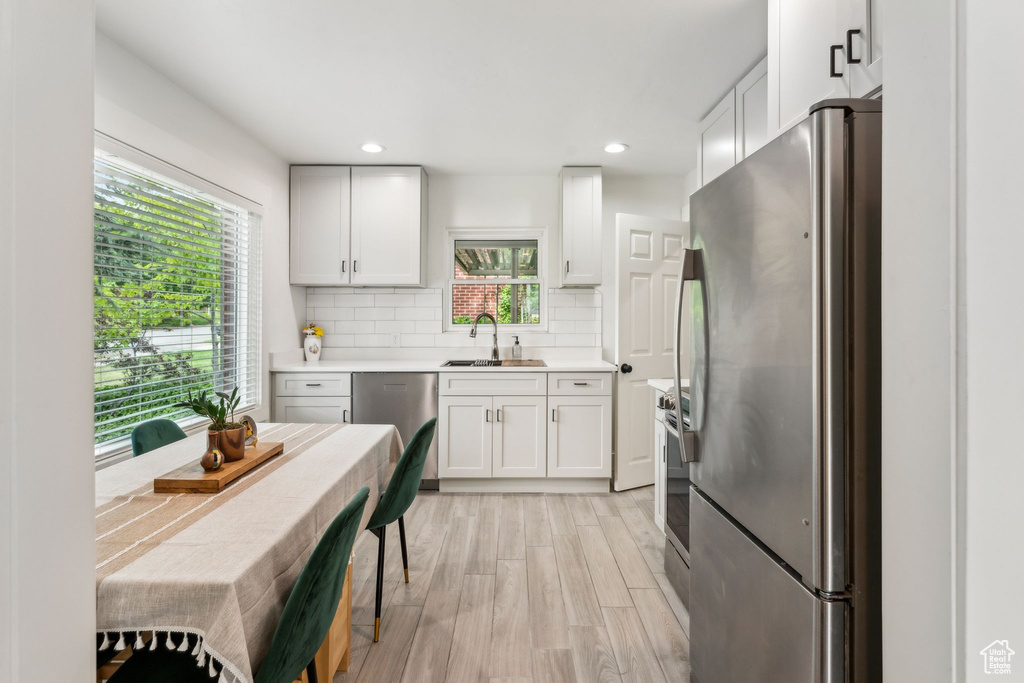 Kitchen with stainless steel appliances, a sink, light wood finished floors, tasteful backsplash, and light countertops