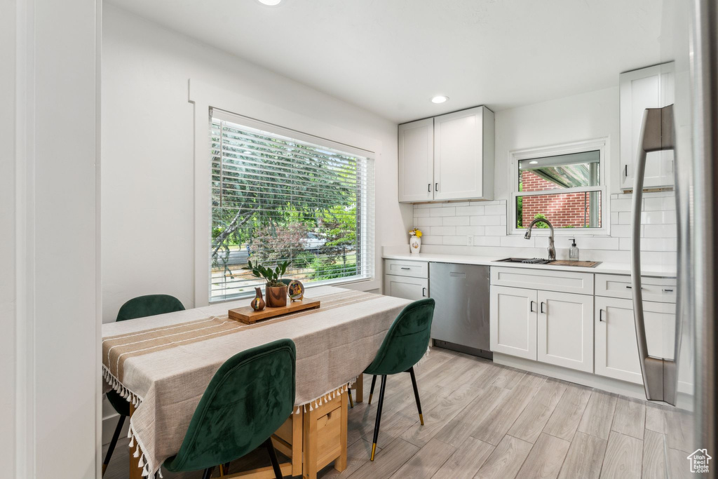 Kitchen with stainless steel dishwasher, a sink, light countertops, tasteful backsplash, and light wood-type flooring