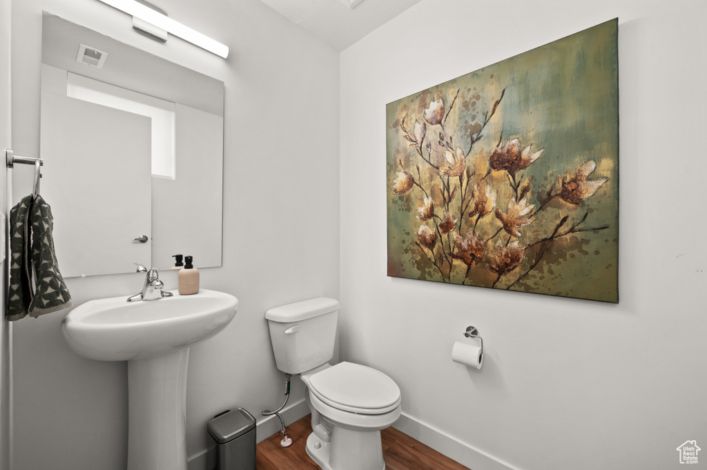 Half bath featuring wood finished floors, toilet, and baseboards