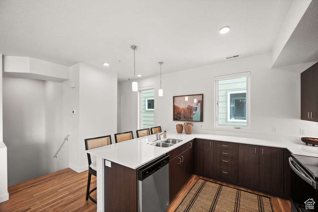 Kitchen with dishwasher, a sink, wood finished floors, electric range, and a kitchen bar