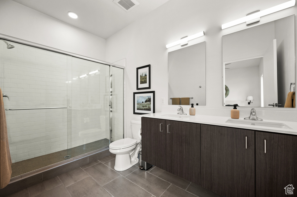Bathroom featuring toilet, double vanity, and a shower stall