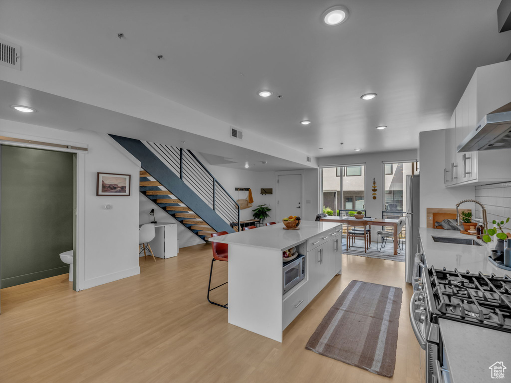 Kitchen with a breakfast bar area, stainless steel appliances, light wood-style floors, a kitchen island, and light countertops