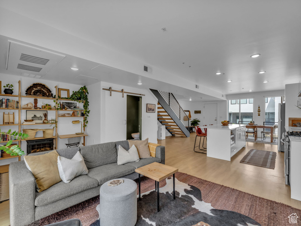 Living room with stairs, a barn door, light wood-style floors, recessed lighting, and a fireplace