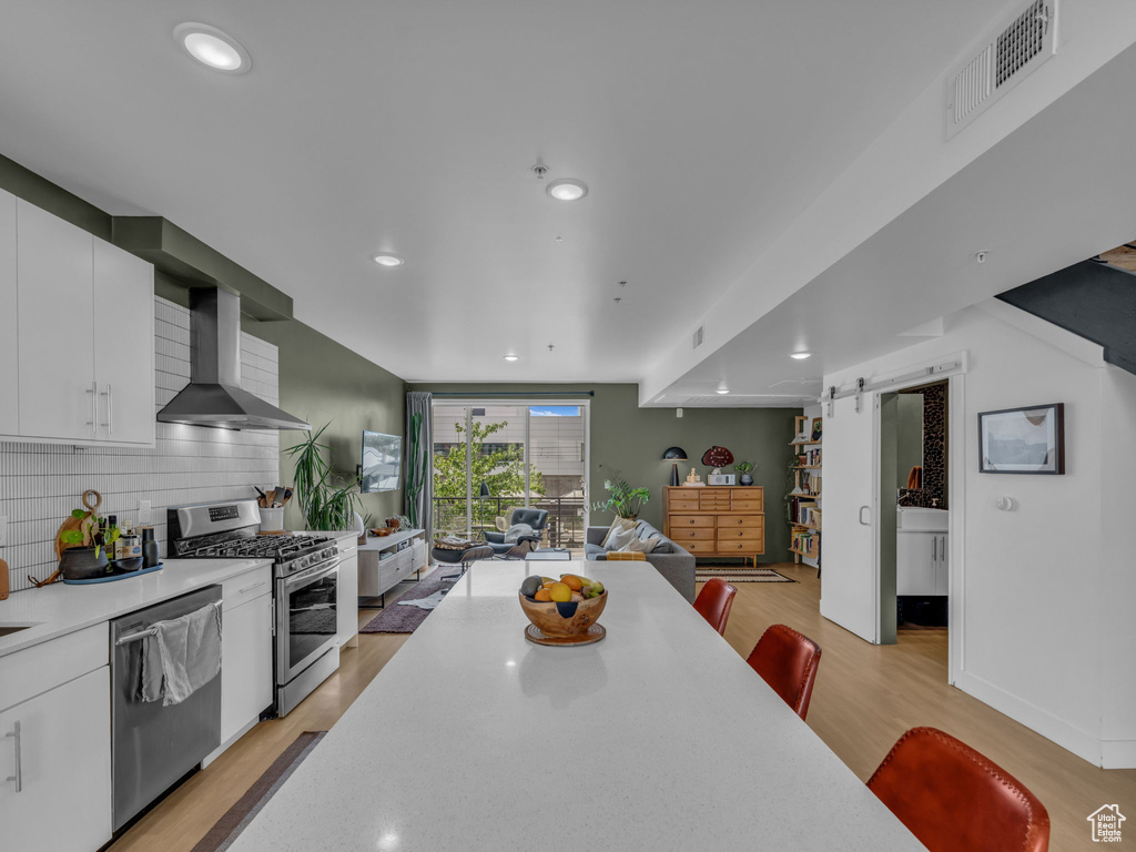 Kitchen featuring appliances with stainless steel finishes, wall chimney exhaust hood, open floor plan, light countertops, and a barn door