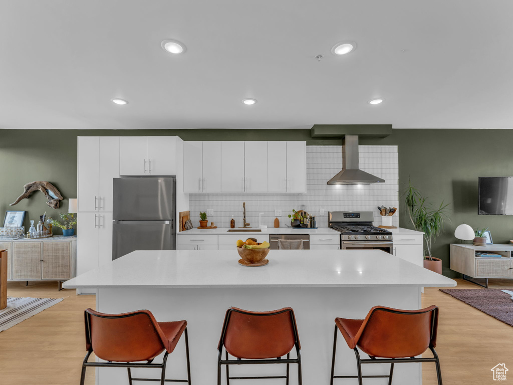 Kitchen featuring appliances with stainless steel finishes, wall chimney range hood, a sink, a breakfast bar, and recessed lighting