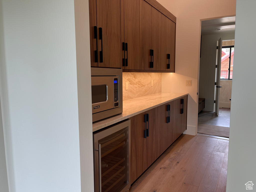 Kitchen featuring wine cooler, stainless steel microwave, light countertops, backsplash, and light wood-style floors