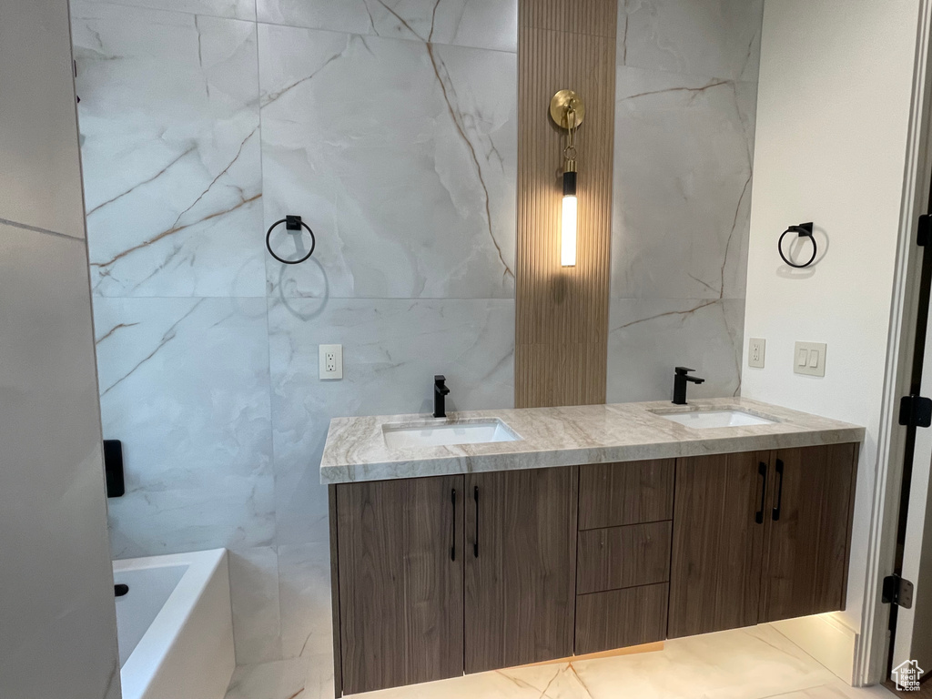 Full bathroom with double vanity, a tub, and tile walls
