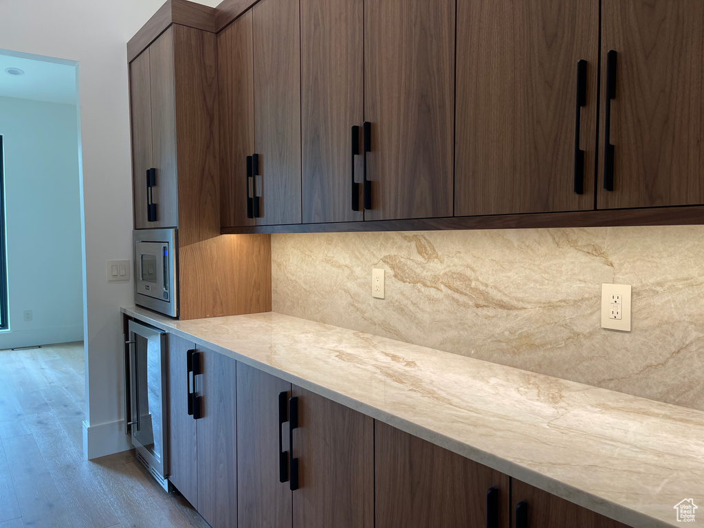 Kitchen with stainless steel microwave, tasteful backsplash, wine cooler, light countertops, and light wood-type flooring