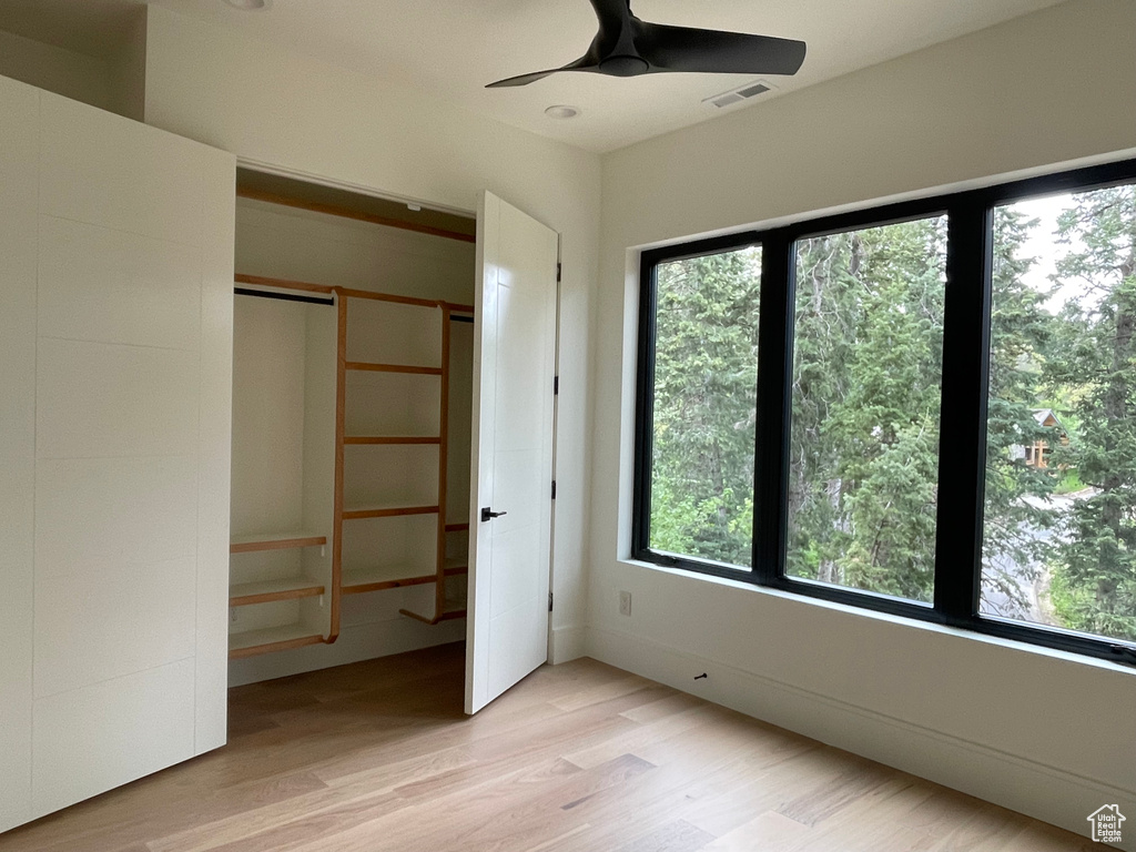 Unfurnished bedroom with multiple windows, light wood-style floors, a closet, and a ceiling fan