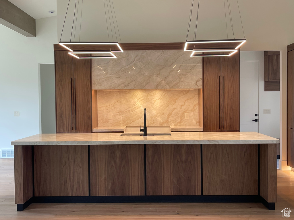 Kitchen with a sink, tasteful backsplash, light wood-type flooring, and a large island with sink