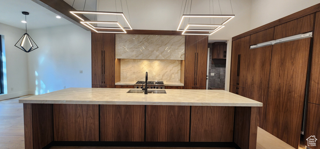 Kitchen featuring light countertops, a sink, backsplash, wood finished floors, and an island with sink