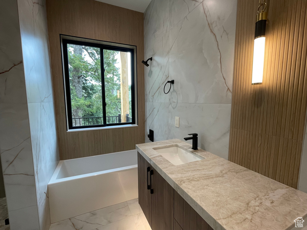 Full bath featuring marble finish floors, a bathtub, vanity, and tile walls