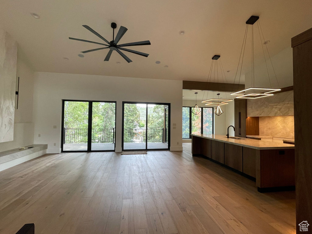 Unfurnished living room featuring a sink, a ceiling fan, light wood finished floors, and a towering ceiling