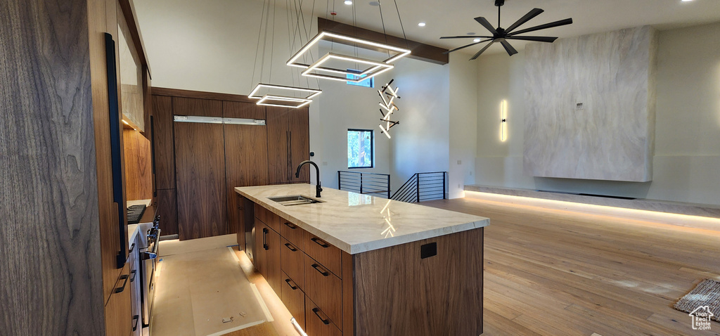 Kitchen with a sink, an island with sink, open floor plan, light wood-style floors, and modern cabinets