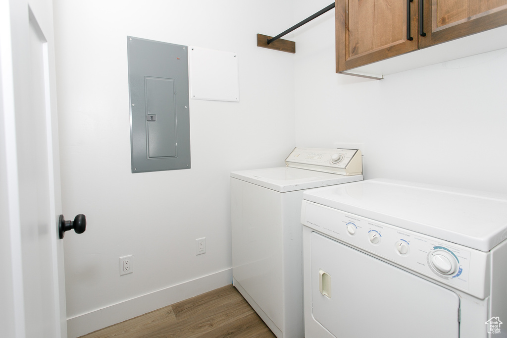 Washroom featuring electric panel, washing machine and dryer, cabinet space, light wood-style floors, and baseboards