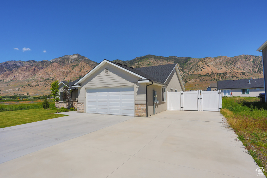 Single story home with a gate, a mountain view, concrete driveway, stone siding, and a garage