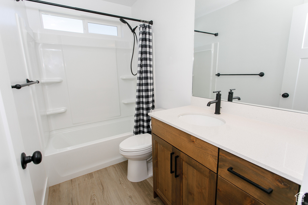 Full bathroom featuring wood finished floors, vanity, shower / tub combo with curtain, and toilet