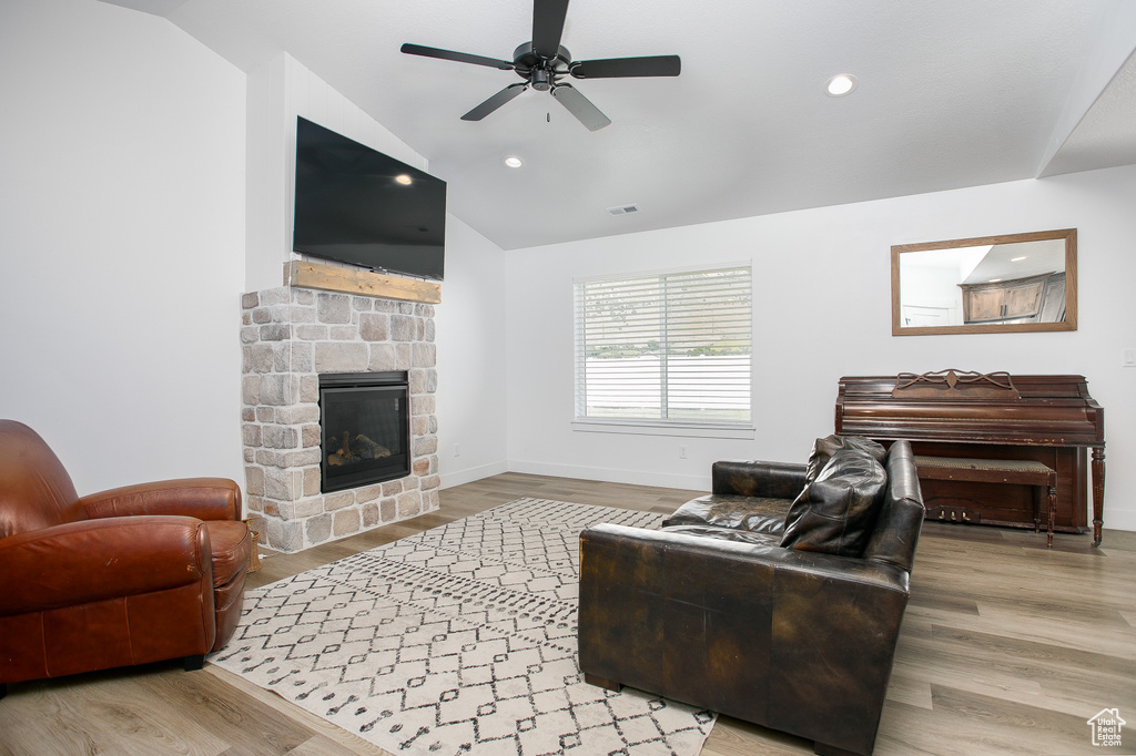 Living room featuring a stone fireplace, lofted ceiling, a ceiling fan, wood finished floors, and baseboards