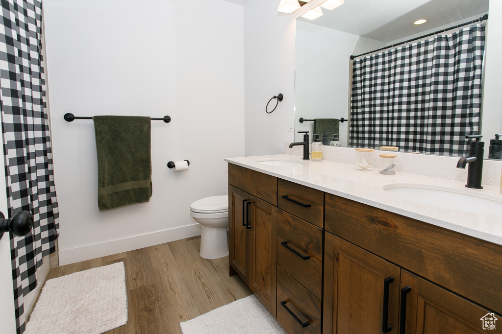 Full bathroom featuring toilet, double vanity, wood finished floors, baseboards, and a shower with curtain