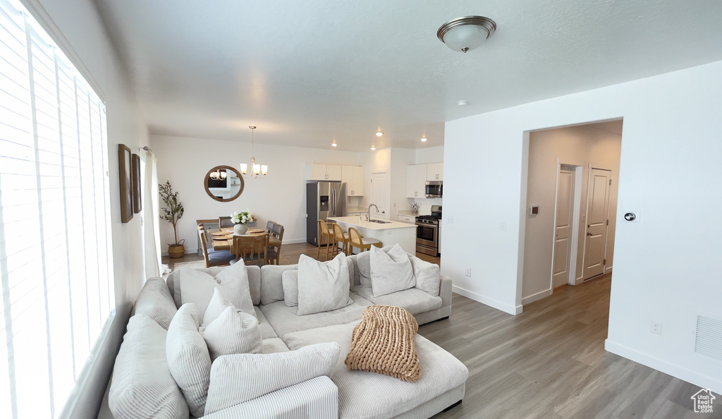Living room featuring a chandelier, light wood finished floors, baseboards, and recessed lighting