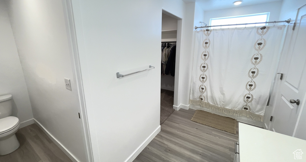 Full bathroom with toilet, wood finished floors, baseboards, and a shower with curtain