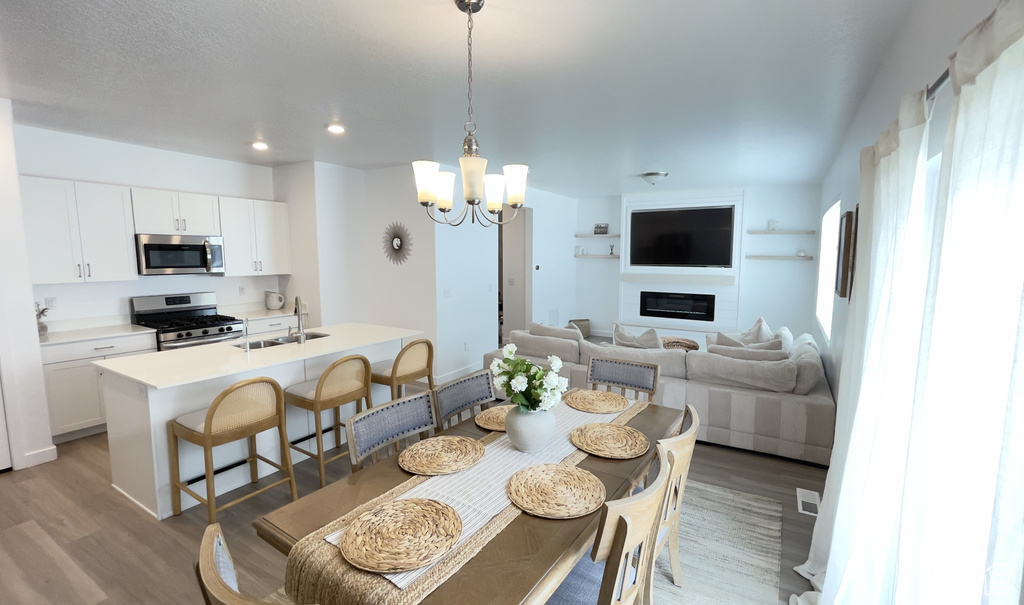 Dining area featuring a chandelier, light wood-style flooring, recessed lighting, and a glass covered fireplace