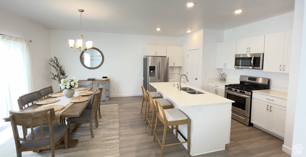 Kitchen with appliances with stainless steel finishes, a sink, wood finished floors, a chandelier, and a breakfast bar