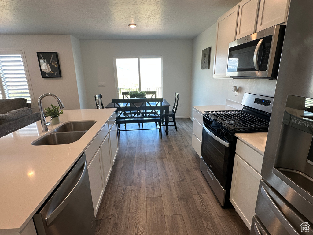Kitchen featuring stainless steel appliances, a sink, plenty of natural light, dark wood-type flooring, and a textured ceiling