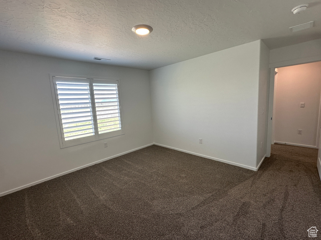 Unfurnished room featuring dark colored carpet, a textured ceiling, a smoke detector, and baseboards