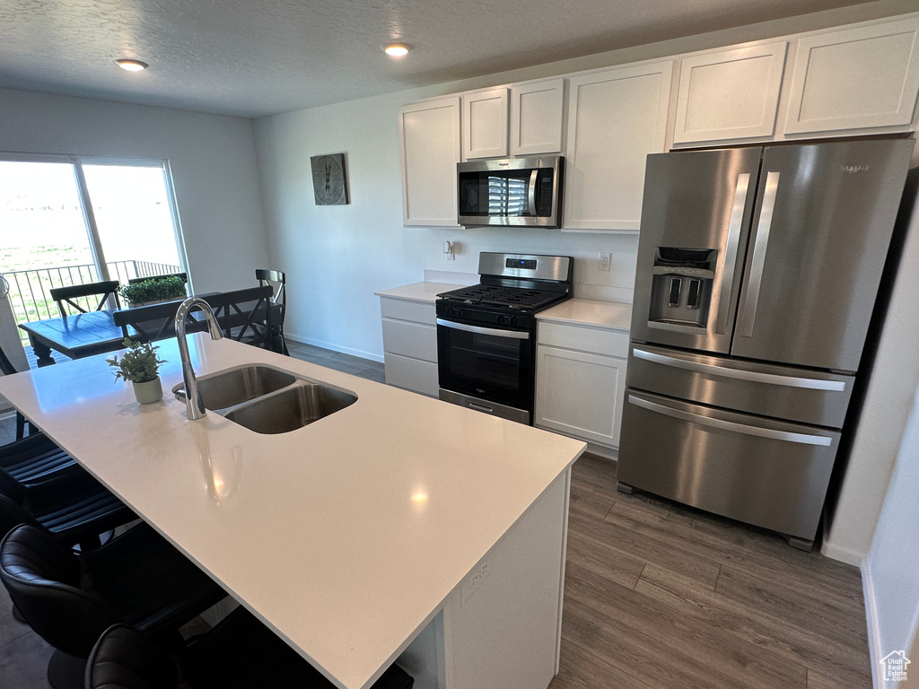 Kitchen with stainless steel appliances, a sink, dark wood-type flooring, light countertops, and a textured ceiling