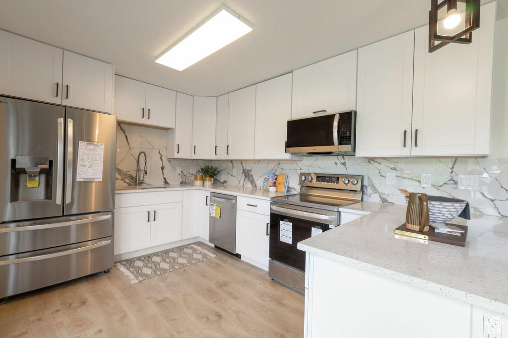 Kitchen featuring appliances with stainless steel finishes, a sink, light wood finished floors, light stone counters, and white cabinets
