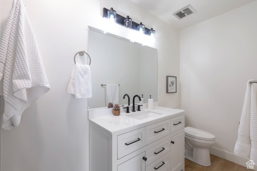Bathroom featuring vanity, toilet, wood finished floors, and baseboards