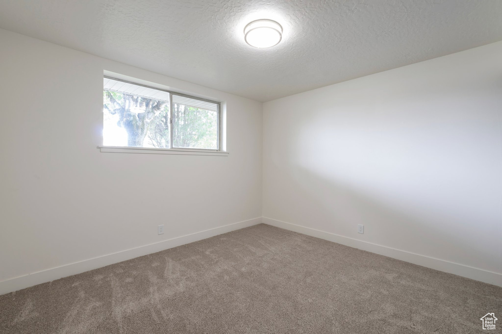 Empty room with light carpet, a textured ceiling, and baseboards