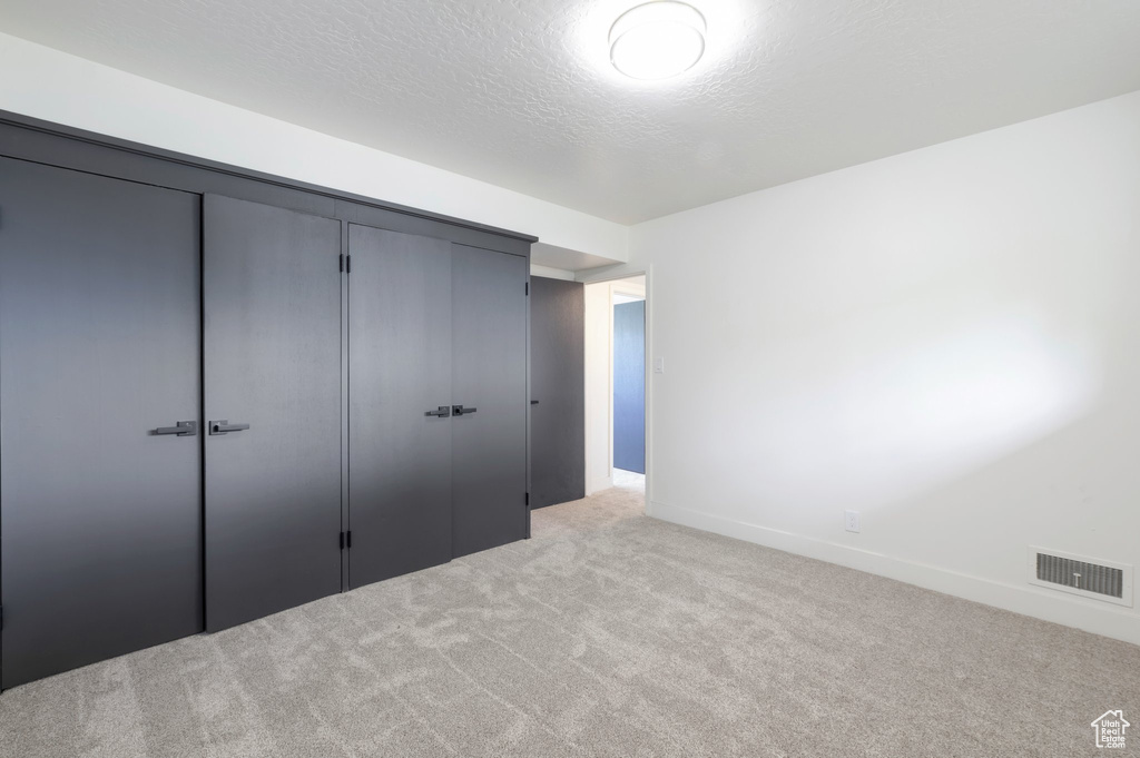 Unfurnished bedroom featuring light carpet, a closet, baseboards, and a textured ceiling