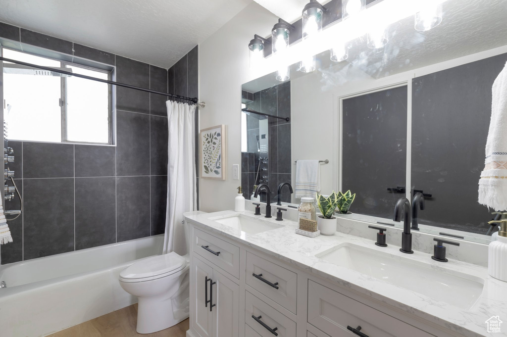 Bathroom featuring double vanity, shower / bath combination with curtain, toilet, and wood finished floors
