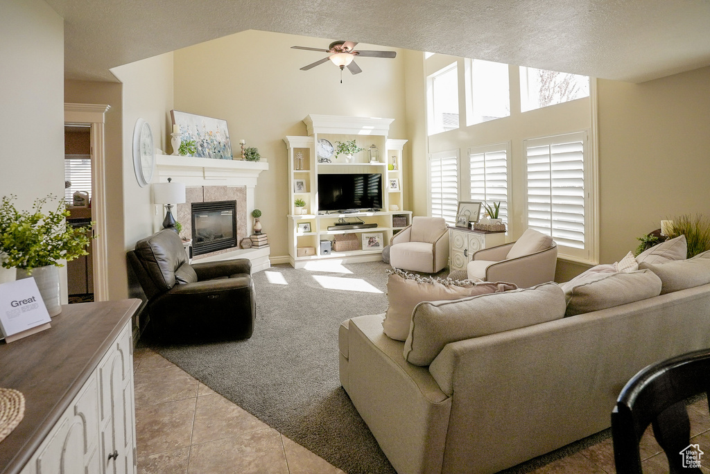 Living area featuring ceiling fan, a tiled fireplace, light carpet, light tile patterned floors, and a textured ceiling