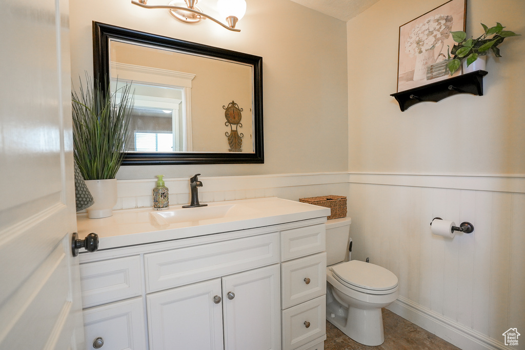Half bath with toilet, vanity, and a wainscoted wall
