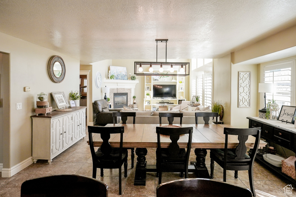 Dining space featuring healthy amount of natural light, a textured ceiling, a fireplace, baseboards, and light tile patterned floors