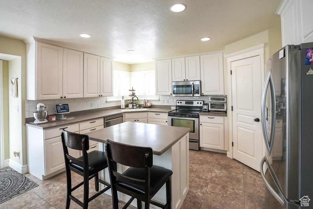 Kitchen featuring appliances with stainless steel finishes, dark countertops, a sink, backsplash, and a kitchen breakfast bar