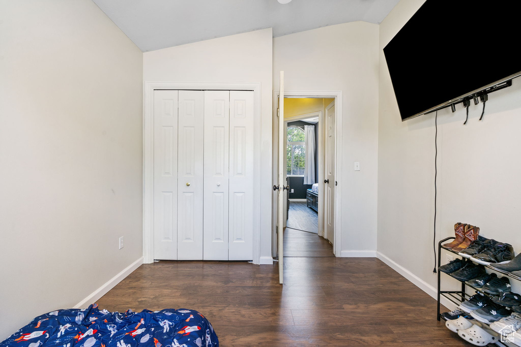 Bedroom with lofted ceiling, wood finished floors, baseboards, and a closet