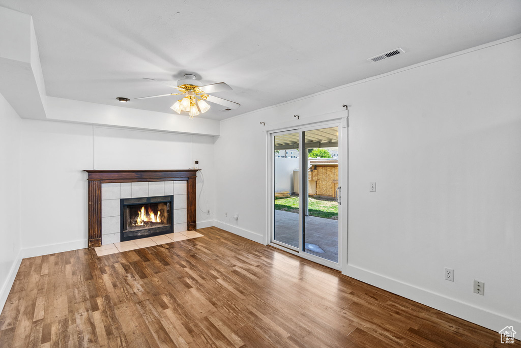 Unfurnished living room with wood finished floors, baseboards, a tiled fireplace, and ceiling fan