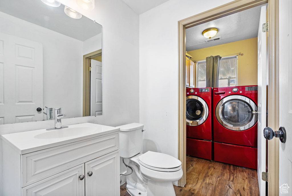 Bathroom featuring washer and clothes dryer, vanity, wood finished floors, and toilet